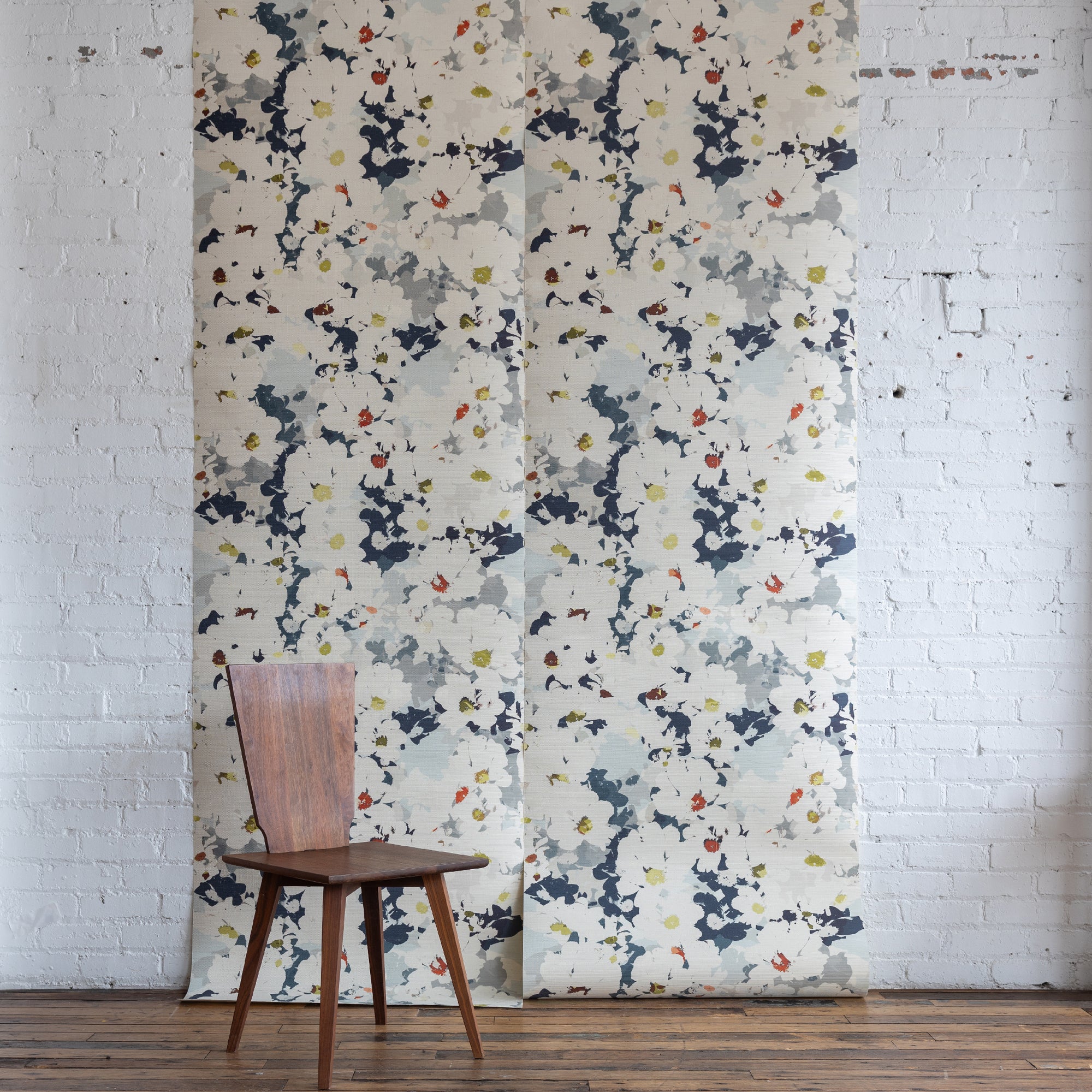 Grasscloth wallpaper of a large floral printed on grasscloth, staged on a white brick wall with a wooden chair
