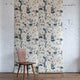 Grasscloth wallpaper of a large floral printed on grasscloth, staged on a white brick wall with a wooden chair