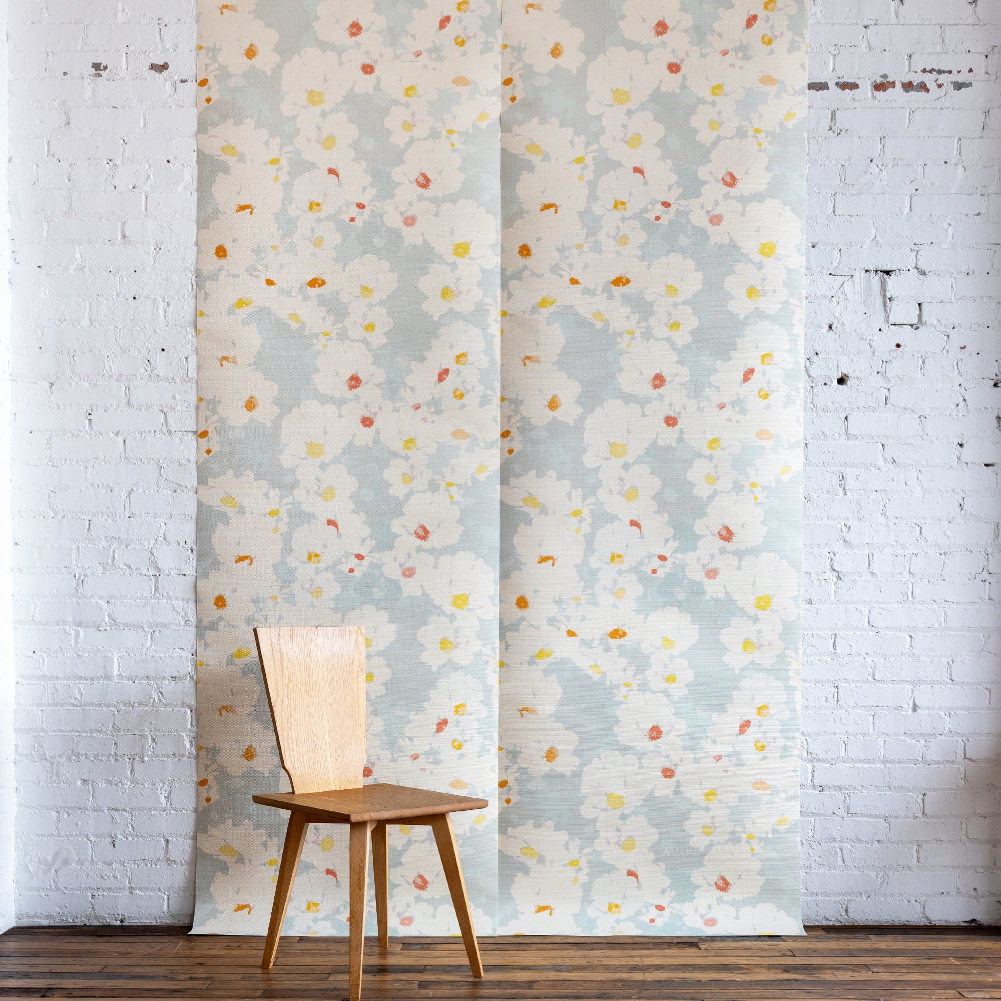 Floral grasscloth wallpaper with a wooden chair and lamp against a white brick wall.