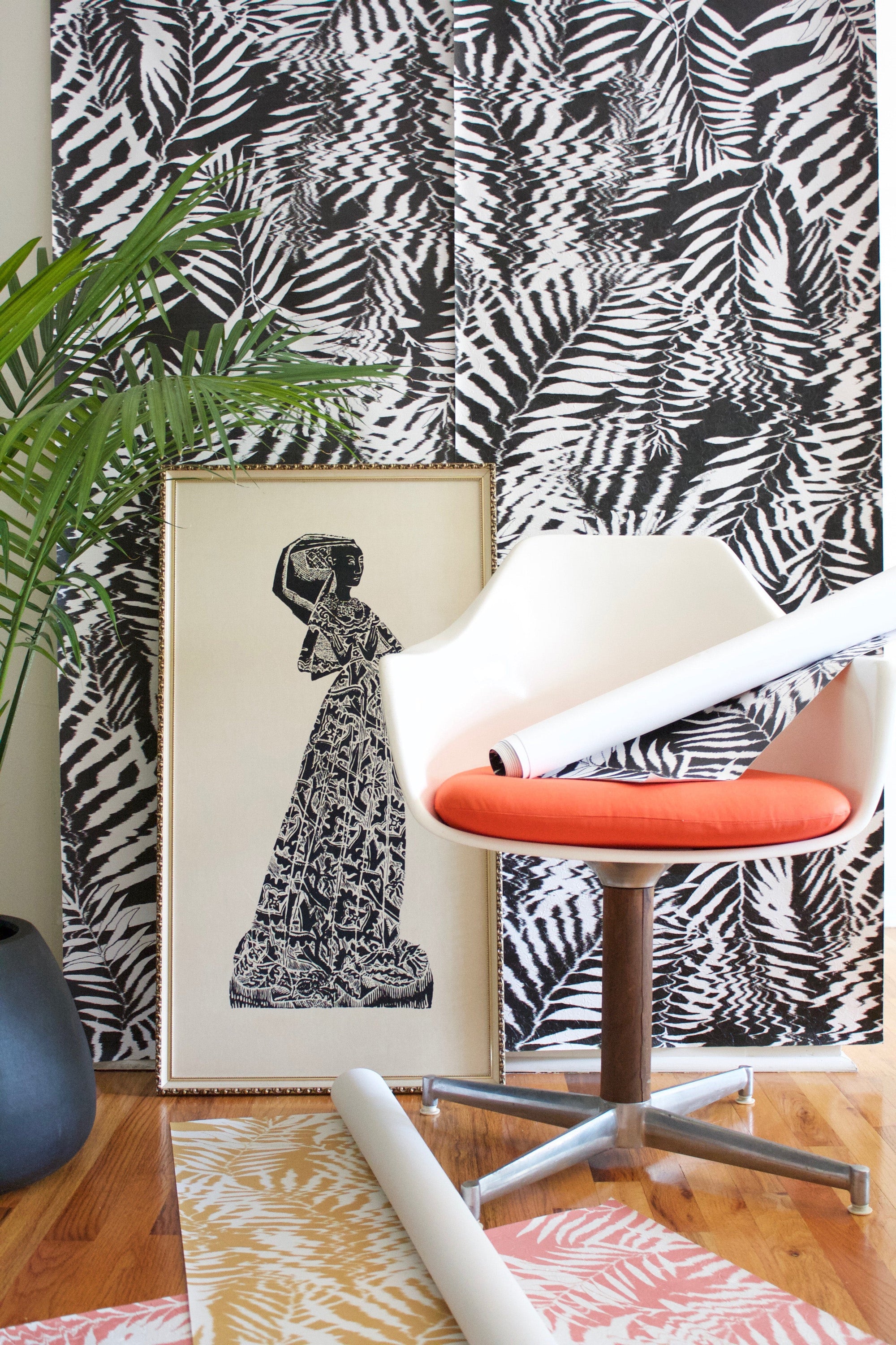 Bold black and white tropical leaf wallpaper with a distorted, ripple-like effect, styled with a modern white chair and vibrant orange cushion.