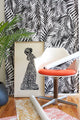 Bold black and white tropical leaf wallpaper with a distorted, ripple-like effect, styled with a modern white chair and vibrant orange cushion.
