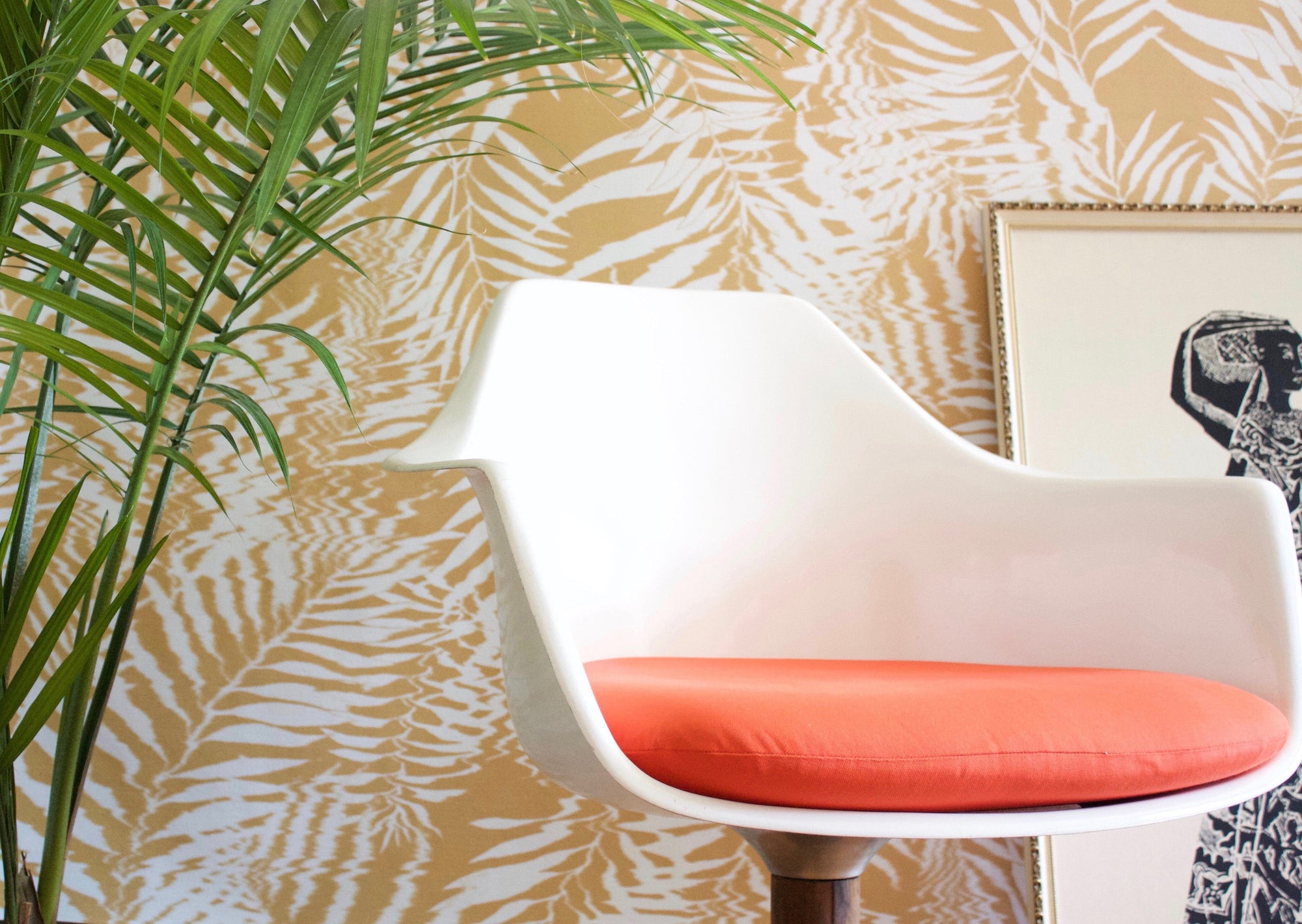 Golden yellow and white tropical leaf wallpaper with a subtle ripple texture, styled with a white modern chair and a potted palm.