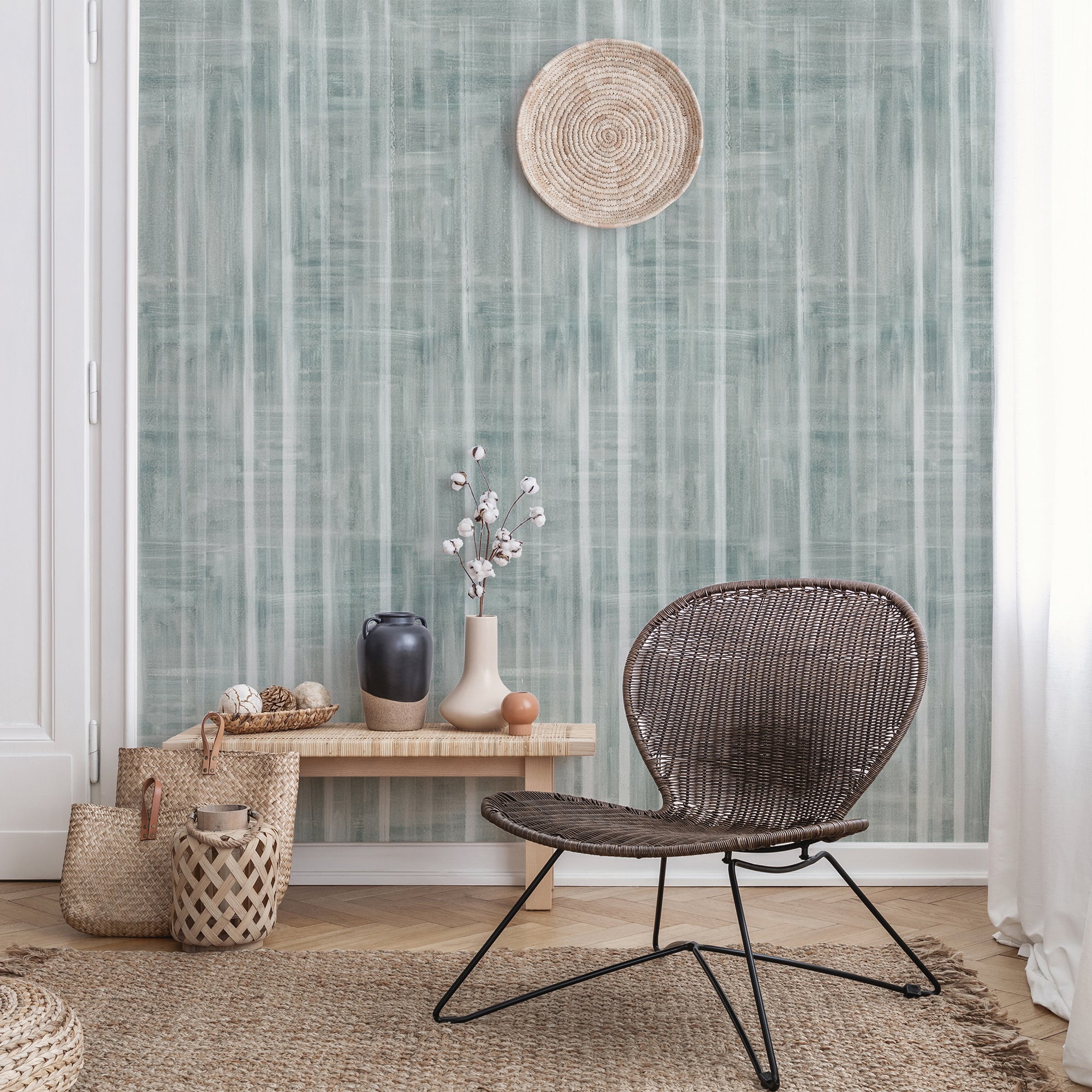 Bohemian-style living room with a green textured wallpaper featuring vertical brushstroke stripes, decorated with woven baskets, vases, and a rattan chair.