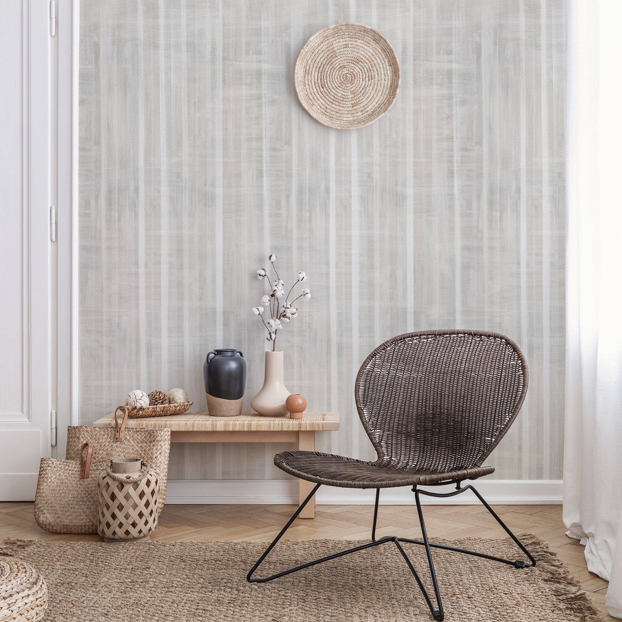 Bohemian-style living room with a soft beige textured wallpaper featuring vertical brushstroke stripes, paired with woven baskets, vases, and a rattan chair.