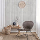 Bohemian-style living room with a soft beige textured wallpaper featuring vertical brushstroke stripes, paired with woven baskets, vases, and a rattan chair.