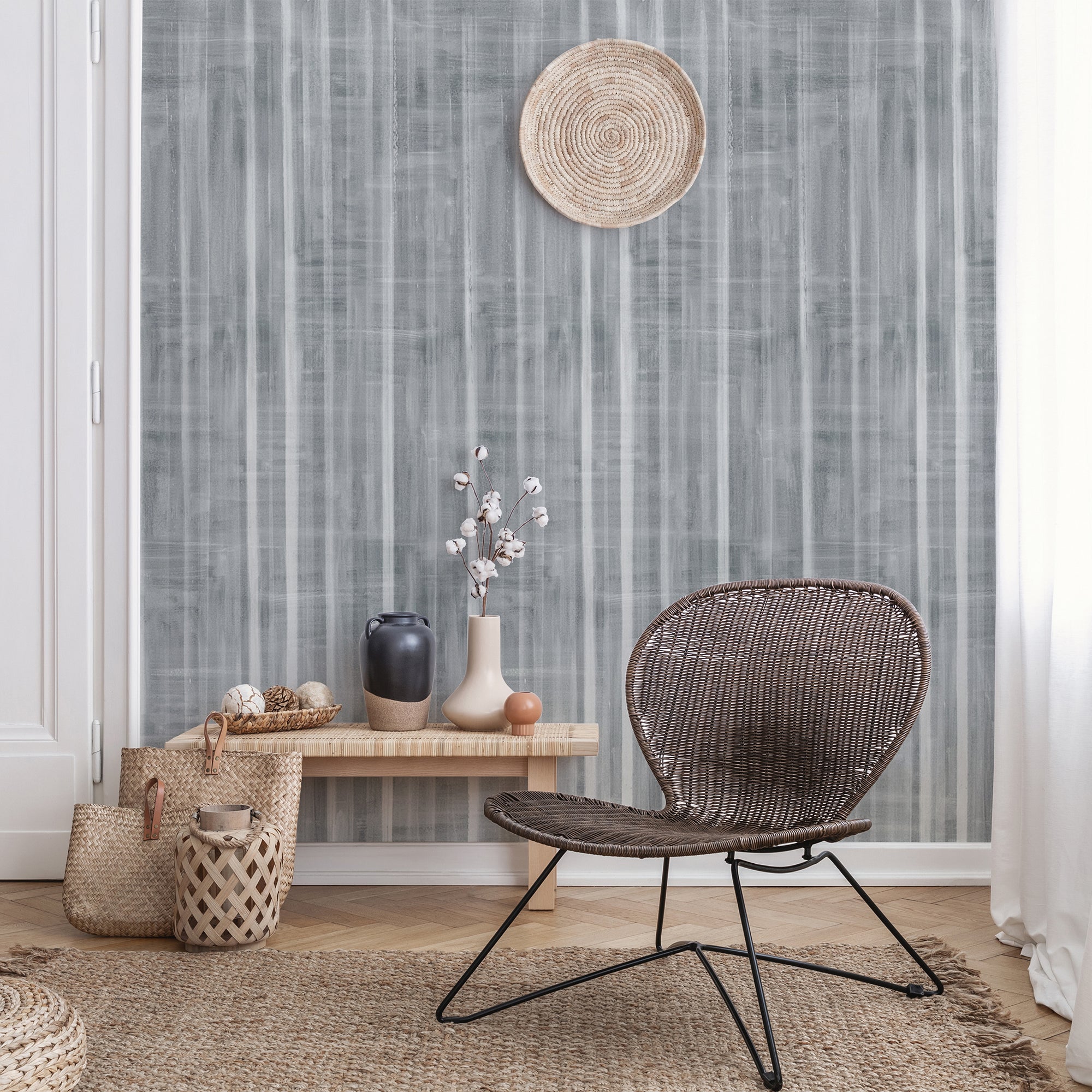 Bohemian-style living room with a deep gray textured wallpaper featuring vertical brushstroke stripes, styled with woven baskets, vases, and a rattan chair.