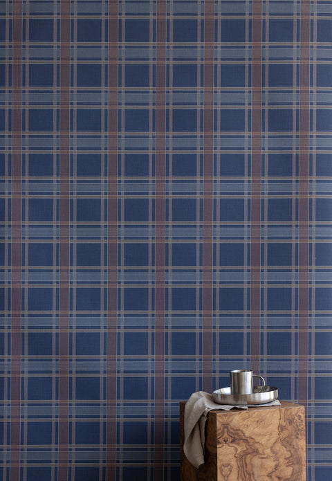 Interior scene with a wooden block side table and metal drinkware in front of a deep navy plaid wallpaper for a cozy, masculine look.