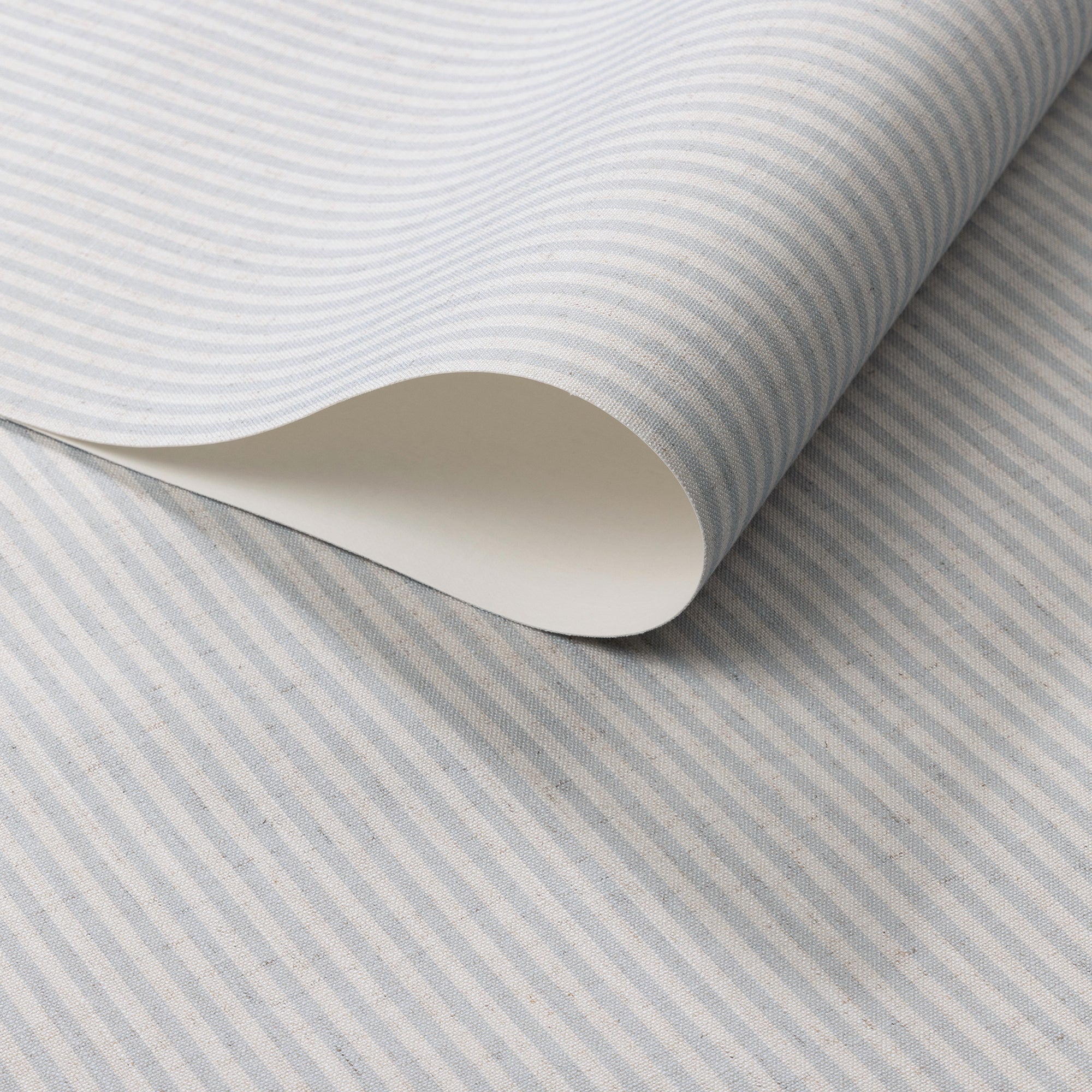 Close-up of a roll of wallpaper with soft blue and ivory vertical pinstripes on a textured linen-like surface.