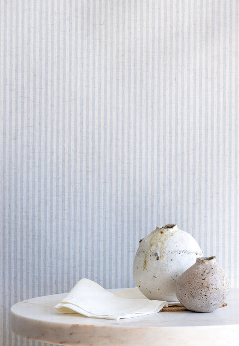 Styled interior scene with textured blue and ivory striped wallpaper as a backdrop, complemented by a marble table and two rustic ceramic vases.
