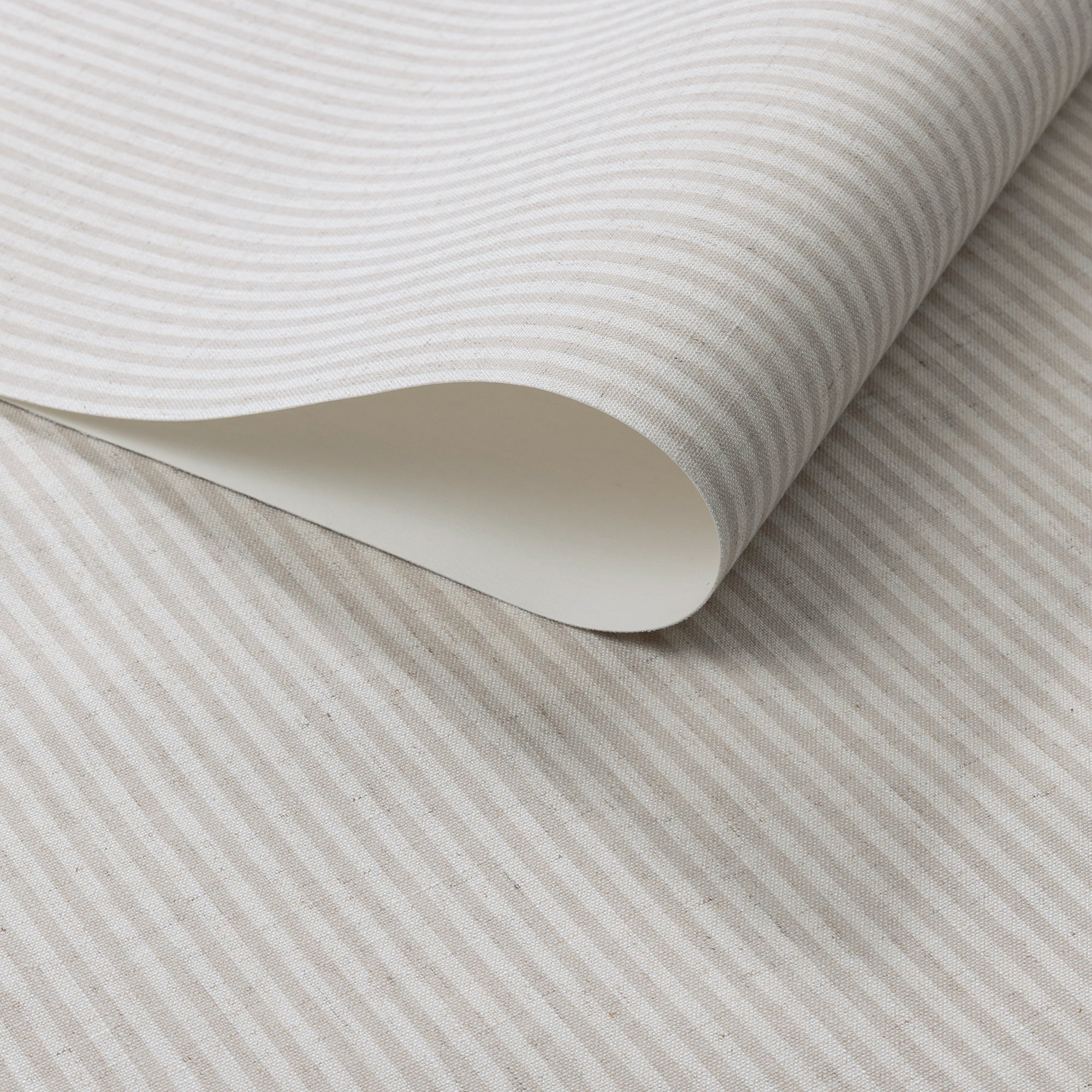 Close-up of wallpaper roll with vertical beige and off-white pinstripes, printed on a textured linen surface.