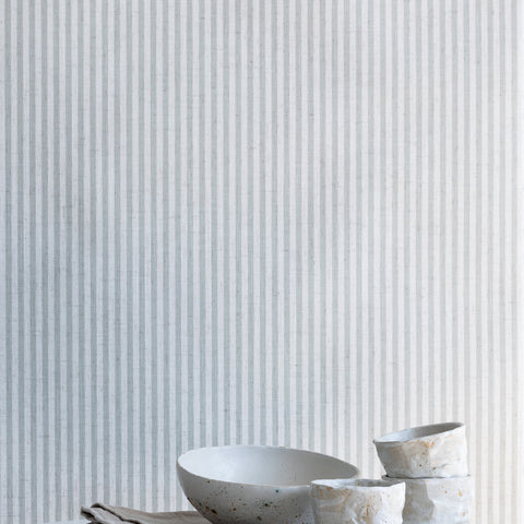 Styled interior scene with sage green and white striped linen wallpaper, paired with a marble tabletop, ceramic bowls, and neutral linens.