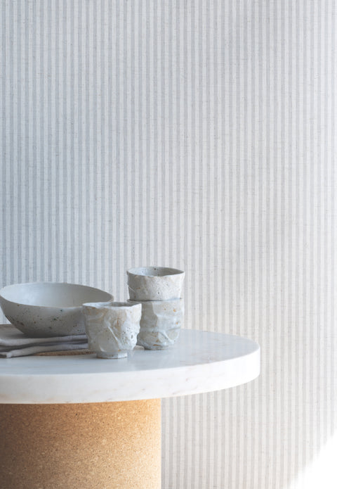 Interior scene with light grey and cream striped wallpaper as a backdrop, paired with a marble table and handmade ceramic cups and bowl.