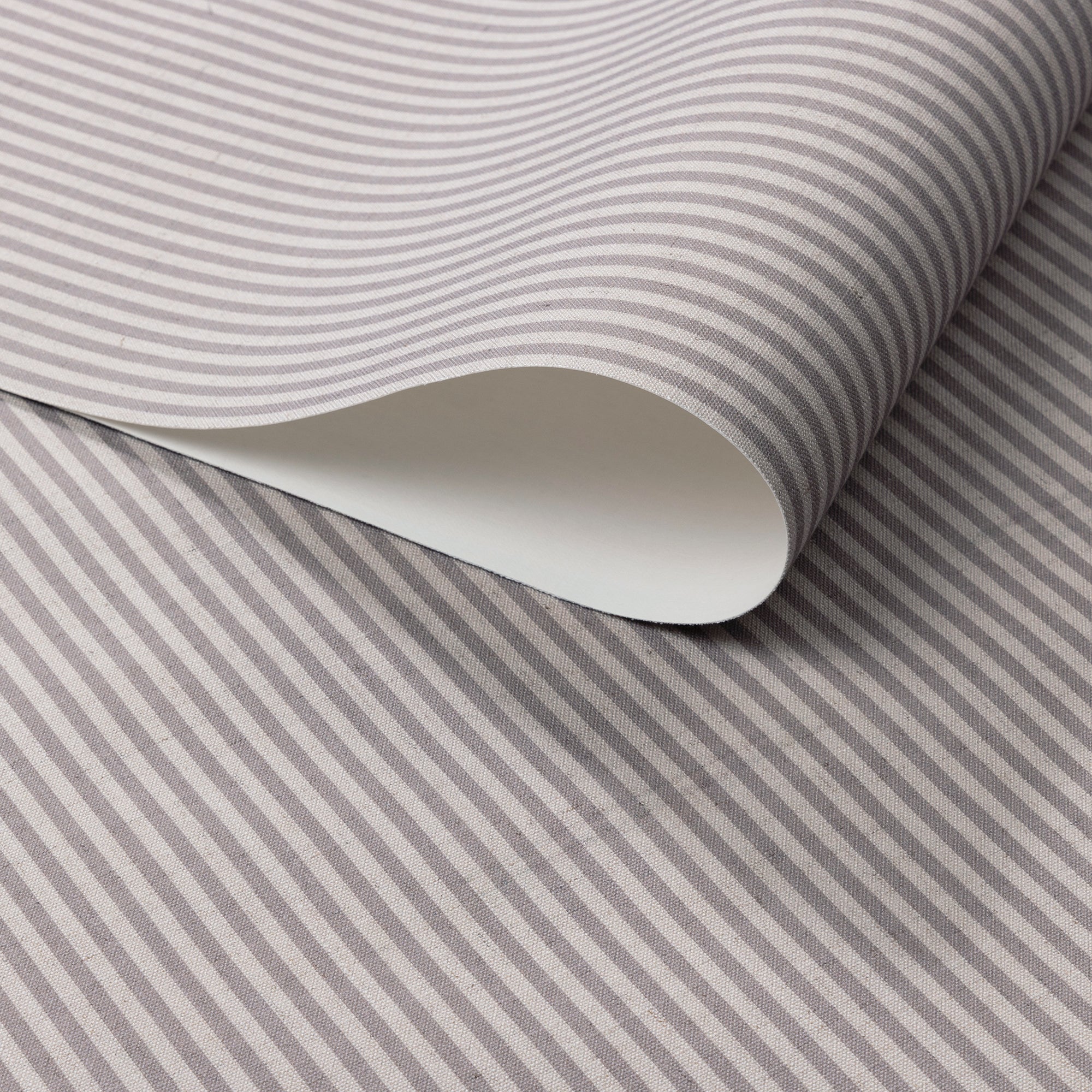 Close-up of folded wallpaper roll with classic charcoal and cream vertical pinstripes, printed on a textured linen.