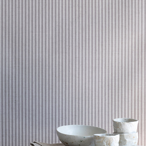Interior scene with charcoal-striped linen wallpaper behind a marble table styled with handmade ceramic cups and a neutral linen napkin.