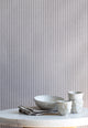 Interior scene with charcoal-striped linen wallpaper behind a marble table styled with handmade ceramic cups and a neutral linen napkin.