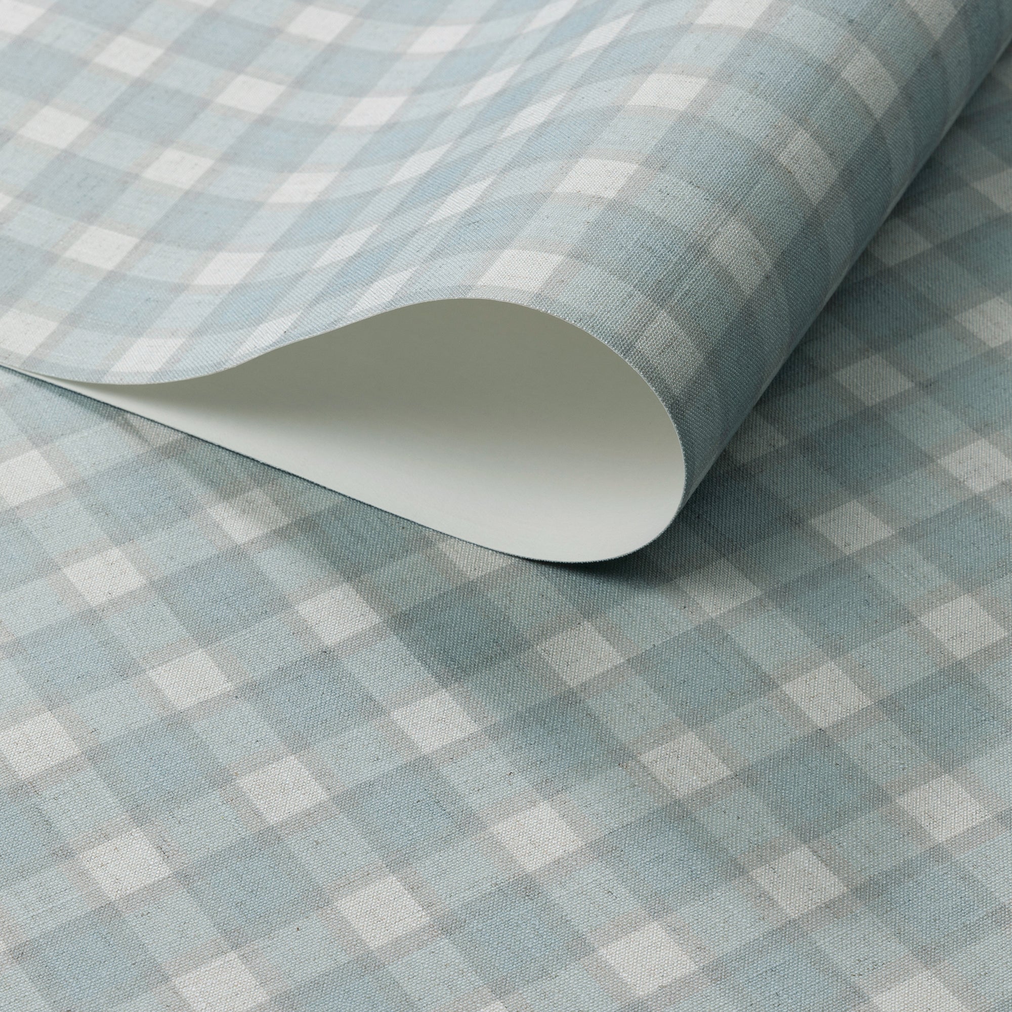 Close-up of a rolled sheet of vintage-style plaid check wallpaper in soft blue and white tones with a linen-textured finish.