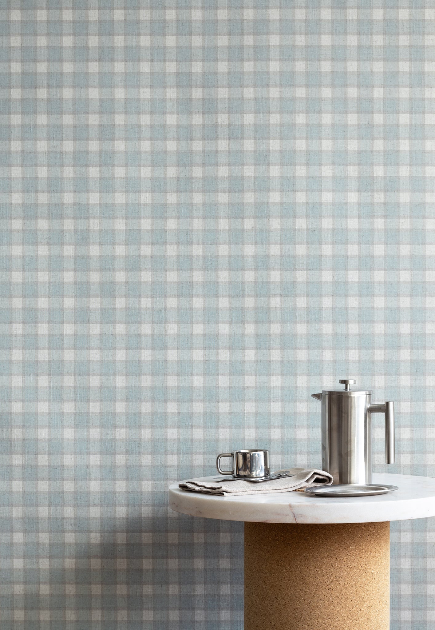 Interior setting with vintage blue and white plaid check wallpaper as the backdrop, styled with a marble and cork pedestal table and stainless steel coffee accessories.