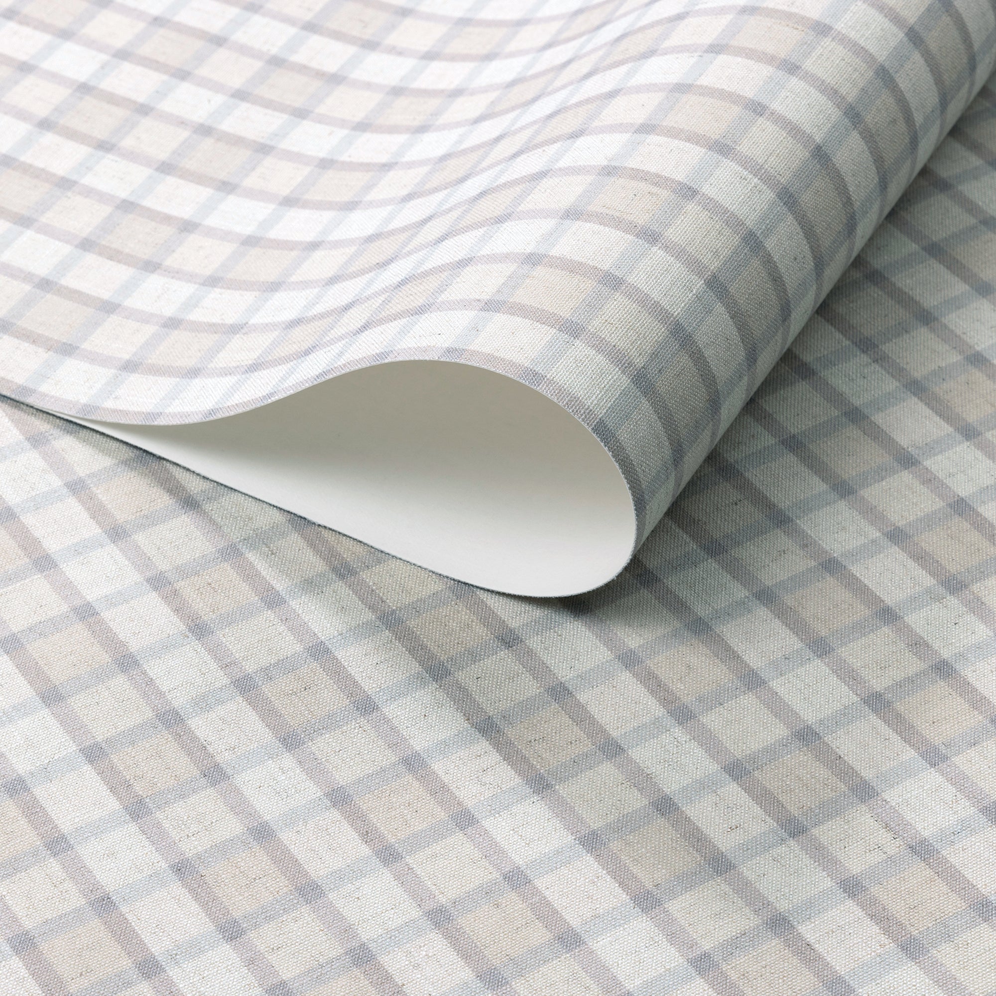 Close-up of vintage plaid check wallpaper in soft beige and grey-blue tones with a linen surface, partially rolled to show paper thickness.