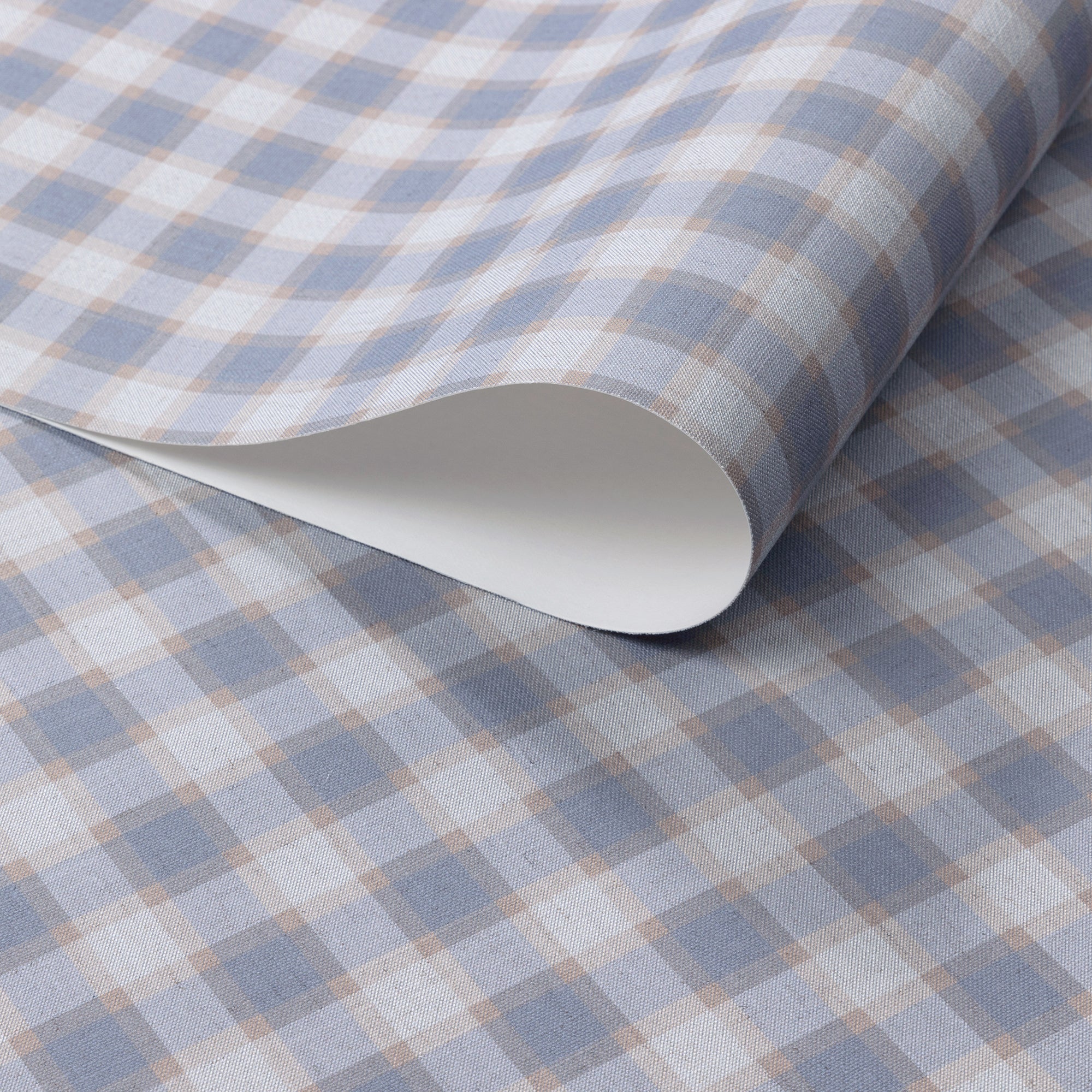 Close-up of vintage plaid check wallpaper in dusty blue and warm beige tones on a soft linen-textured surface, shown with a curled edge to highlight paper quality.