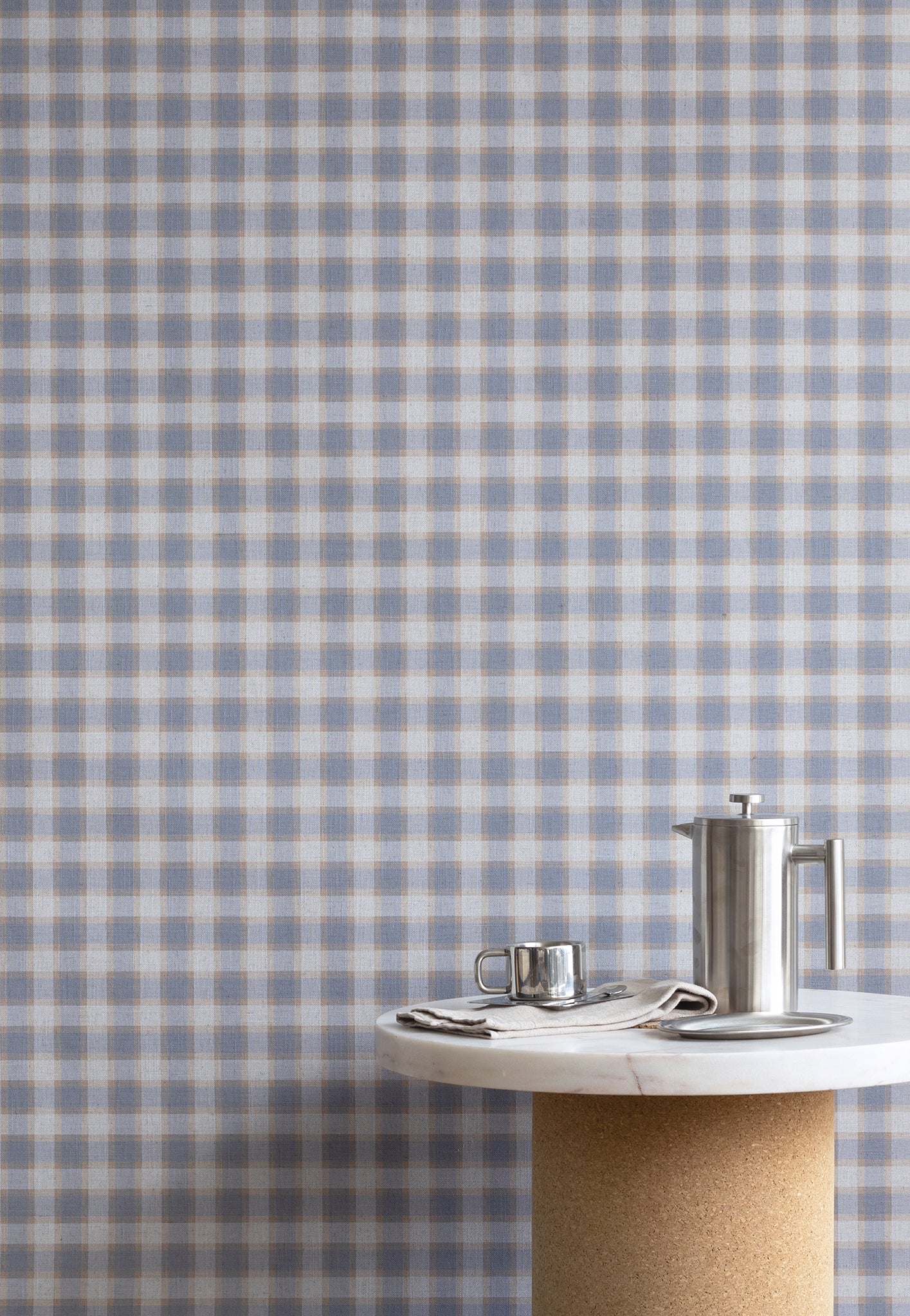 Interior scene with vintage plaid check linen wallpaper in blue and beige tones, styled with a marble and cork table and brushed metal coffee accessories.