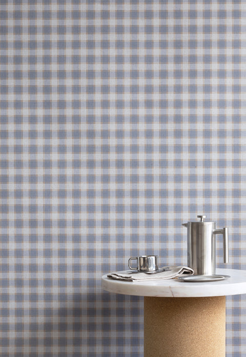 Interior scene with vintage plaid check linen wallpaper in blue and beige tones, styled with a marble and cork table and brushed metal coffee accessories.