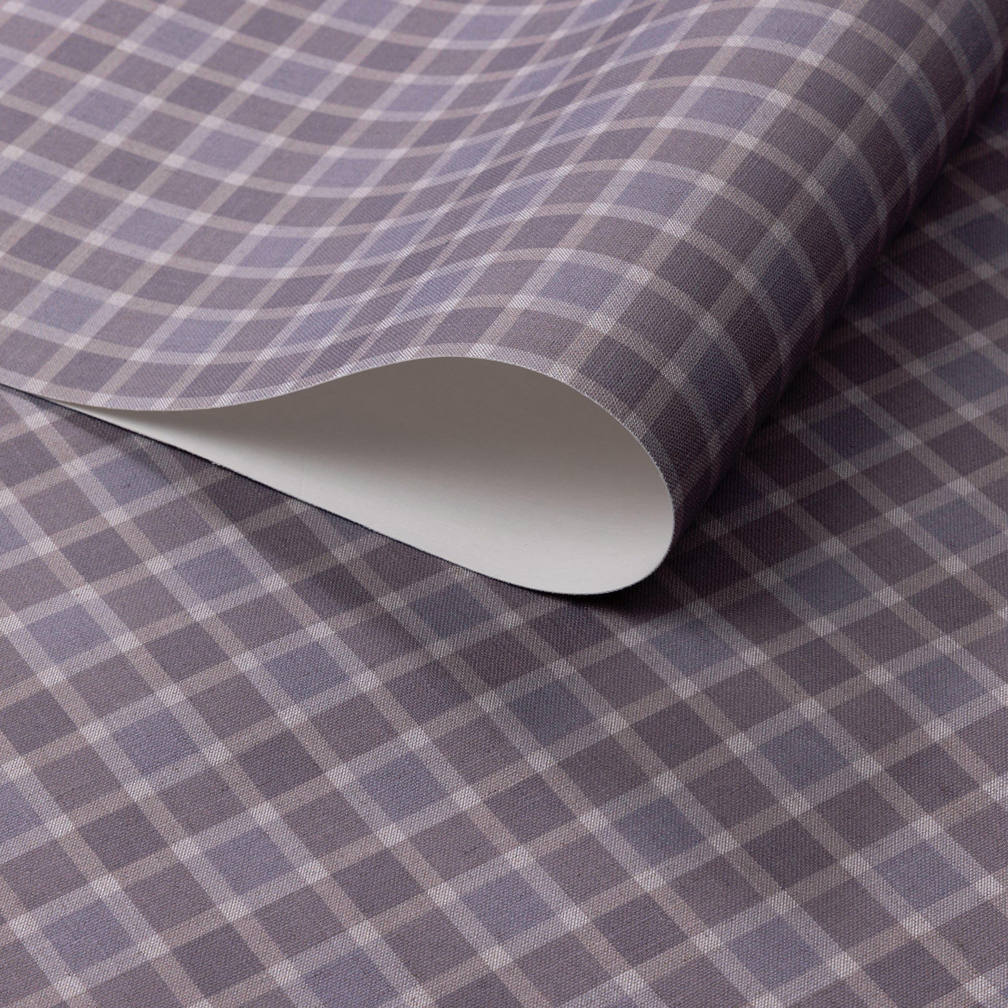 Close-up of vintage plaid check wallpaper in muted lavender and soft taupe tones with a subtle linen-textured finish, shown with a curled edge.