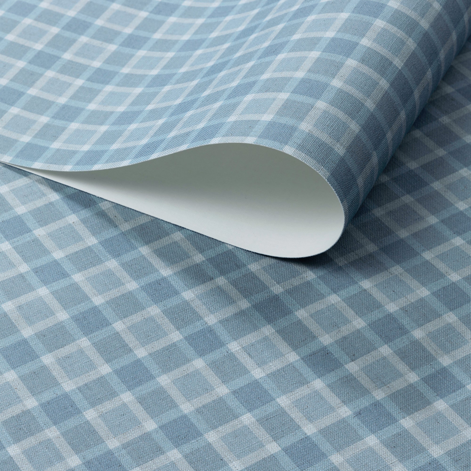 Close-up of vintage plaid check wallpaper in soft blue and ivory tones on a linen-textured surface, with a rolled sheet revealing paper thickness.