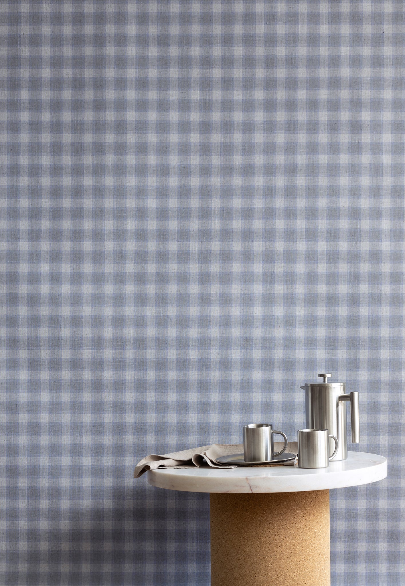 Interior setting with vintage plaid check linen wallpaper in cool gray-blue tones, styled with a marble and cork table and stainless steel coffee set.