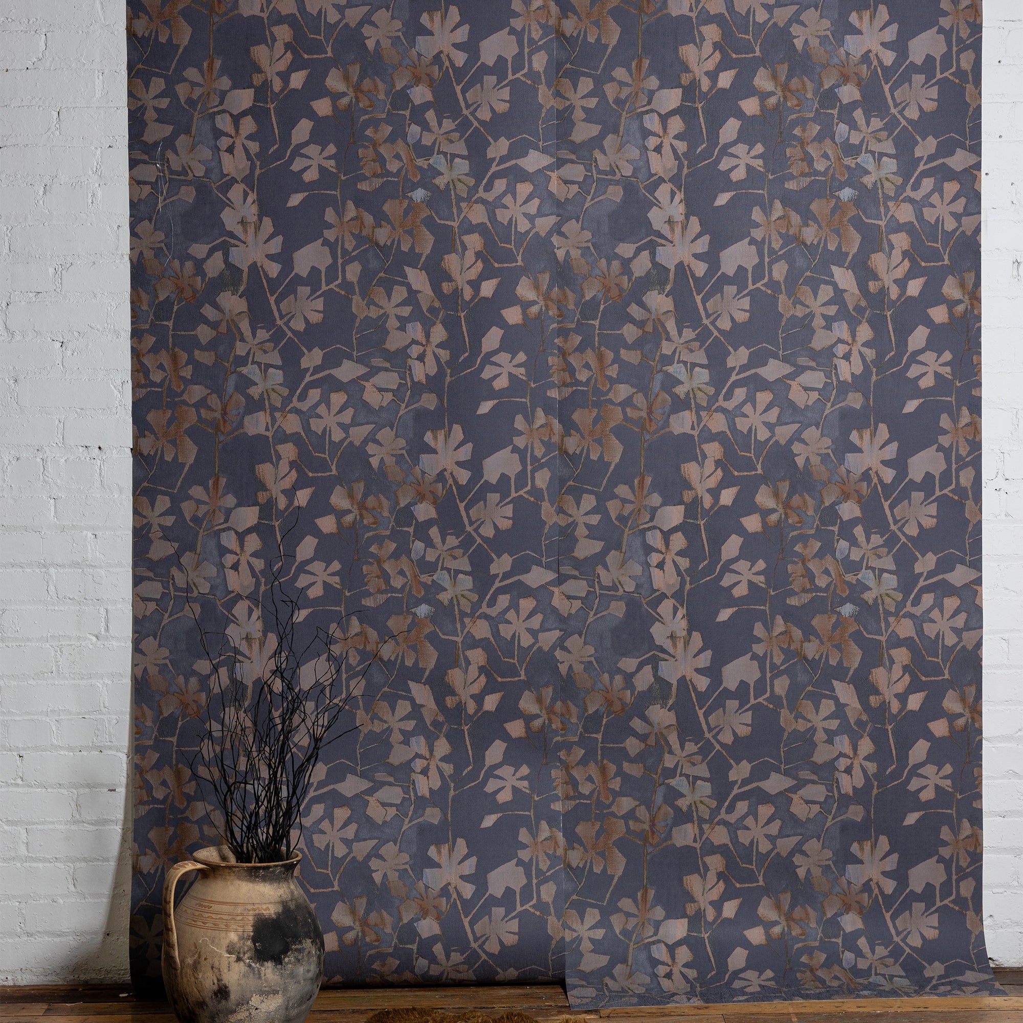 Dark botanical wallpaper with a matte pruple background and muted brown and taupe leafy vine pattern, styled against a white brick wall with a rustic ceramic vase.
