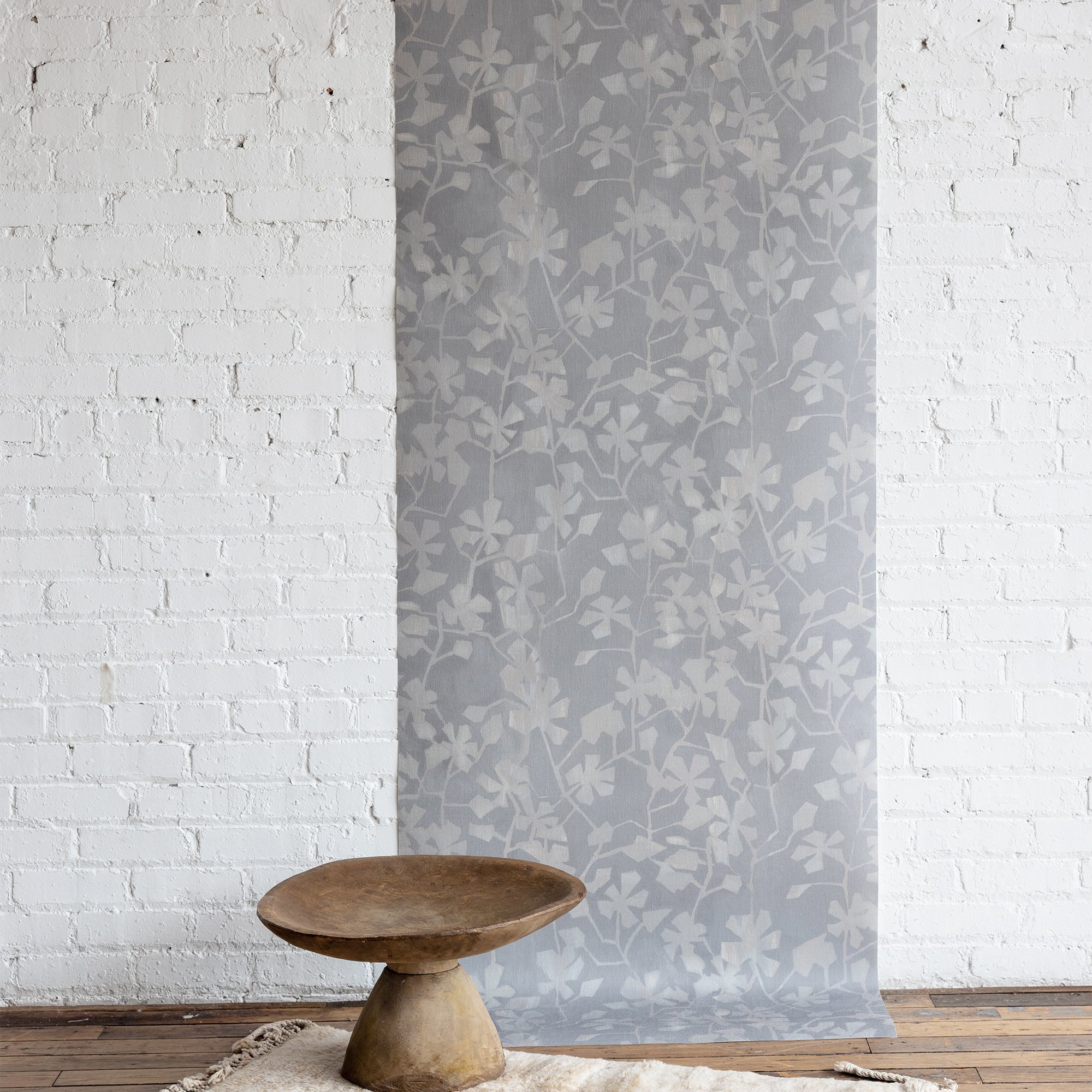 Wallpaper with floral pattern on a white brick wall with a wooden table in front.