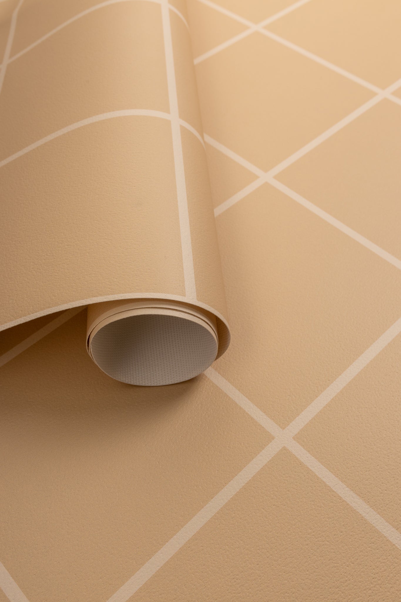 Close-up of a rolled-out beige wallpaper with a white grid pattern, showcasing its textured surface and flexible material.