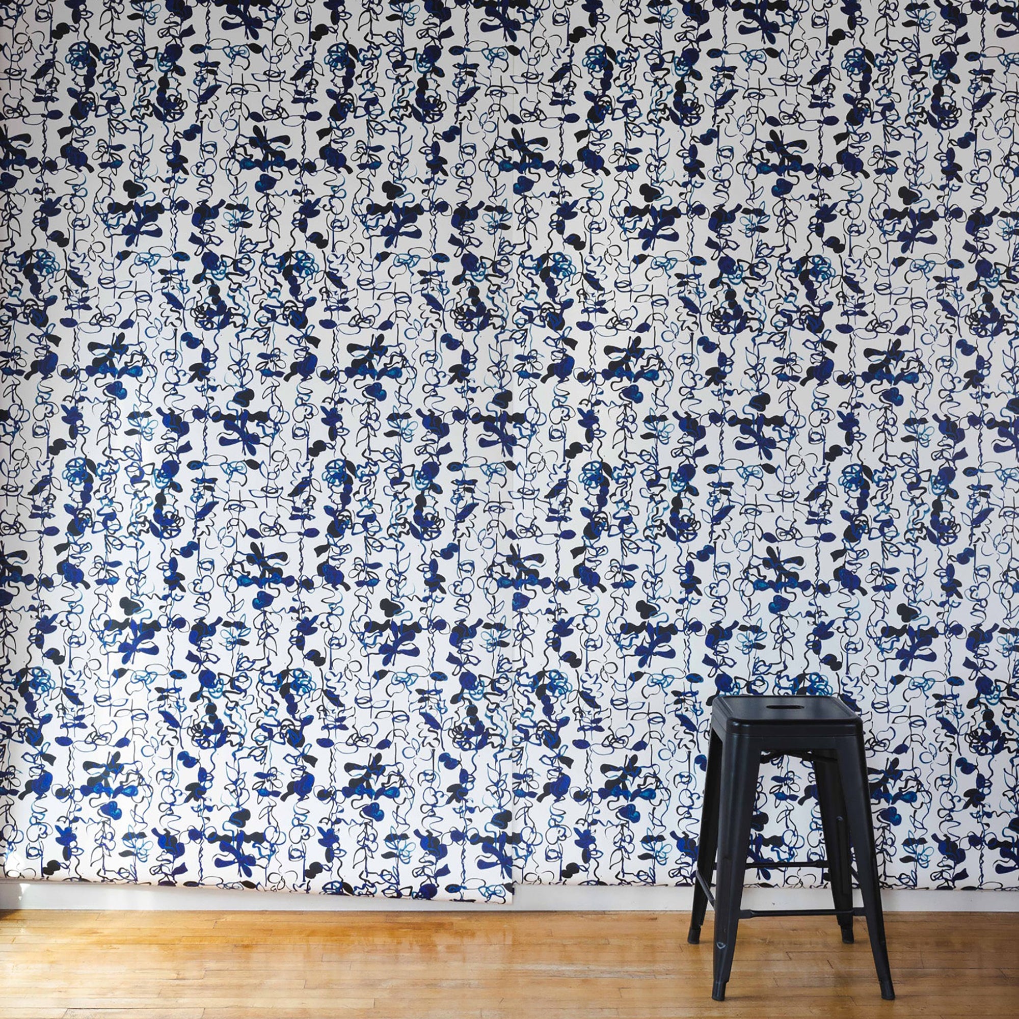 Modern interior featuring a bold abstract floral stripe wallpaper with black and blue hand-drawn botanical elements, paired with a sleek black stool for contrast