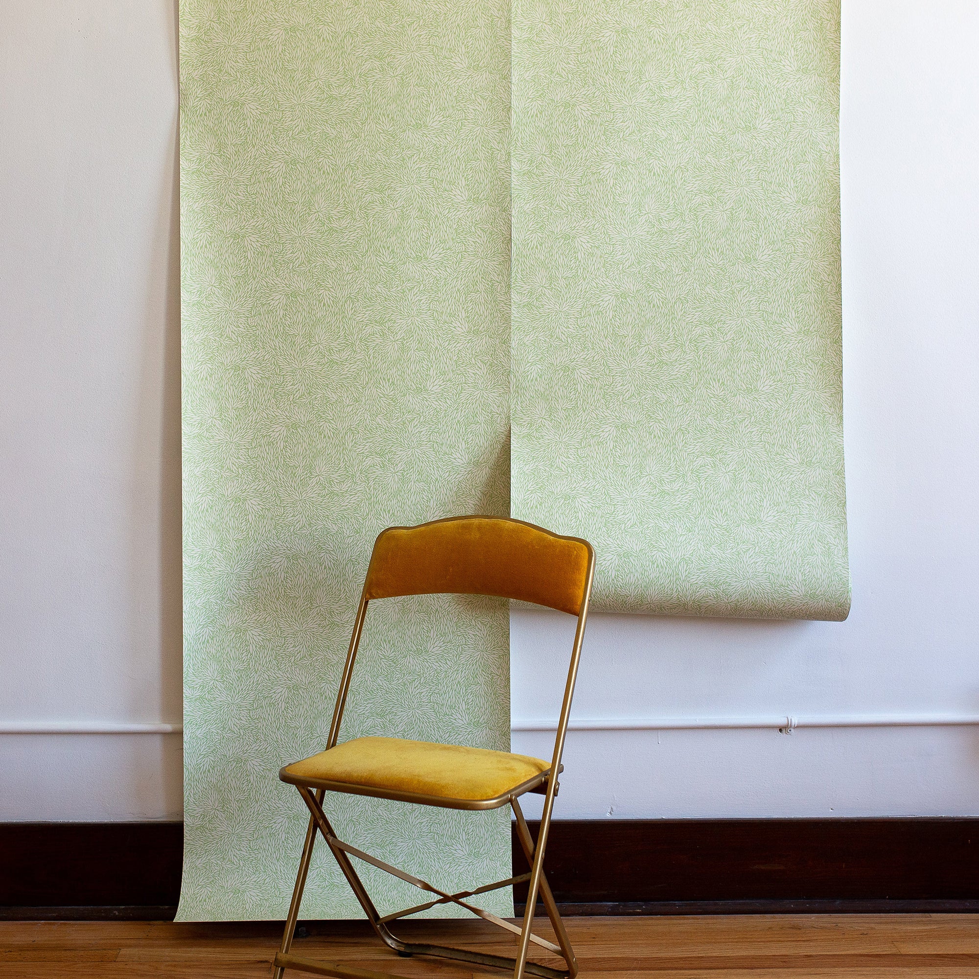 Minimalist interior featuring soft green botanical wallpaper with a fine leaf pattern, paired with a mustard velvet chair for a subtle and elegant contrast.