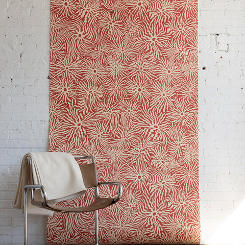 Stylish tan leather and chrome chair draped with a white blanket, placed in front of
red patterned wallpaper with abstract swirling design, on a fluffy cream rug.