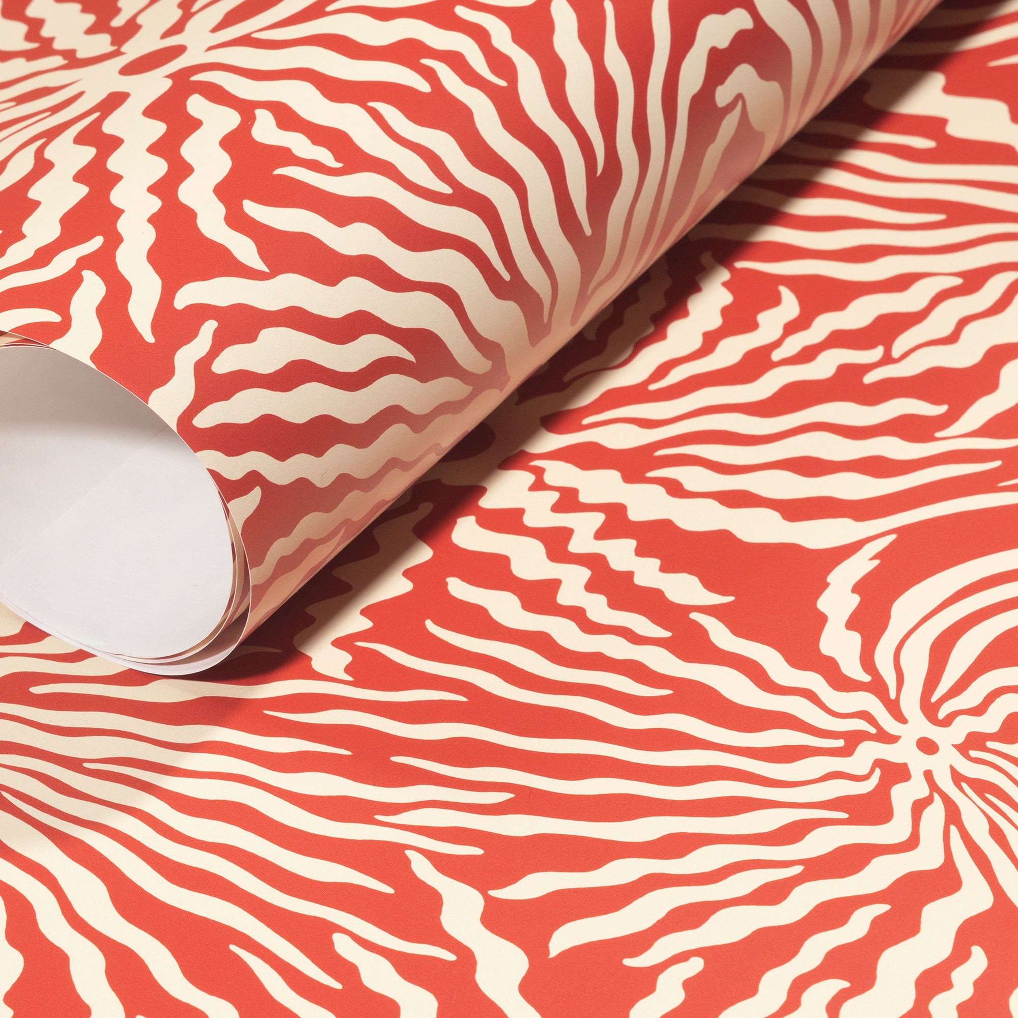 Rolled-up terracotta wallpaper with intricate cream wavy patterns, showcasing its textured, modern appeal.