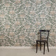 Room with silk wallpaper featuring a delicate botanical design in soft green and beige tones on a white background, depicting hand-painted flowers and leafy vines, complemented by a black wooden chair.