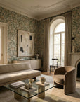 Flora Crème botanical wallpaper in a refined Parisian-style living room with ornate crown molding, arched windows, neutral linen furnishings, and a velvet accent chair — Poppy wallpaper