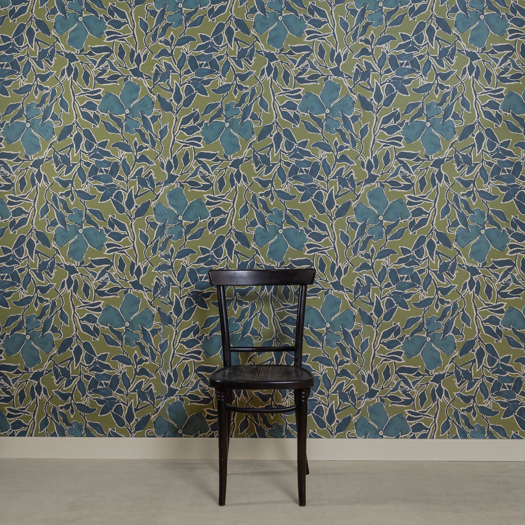 Room with silk wallpaper featuring a bold botanical pattern in deep blue and green tones, showcasing hand-painted flowers and leaves with white outlines, complemented by a black wooden chair in front.