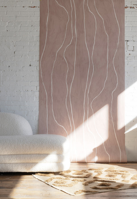 Warm blush wallpaper with organic white vertical lines, styled with a boucle sofa and a beige geometric-pattern rug on a wooden floor.
