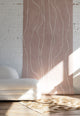 Warm blush wallpaper with organic white vertical lines, styled with a boucle sofa and a beige geometric-pattern rug on a wooden floor.