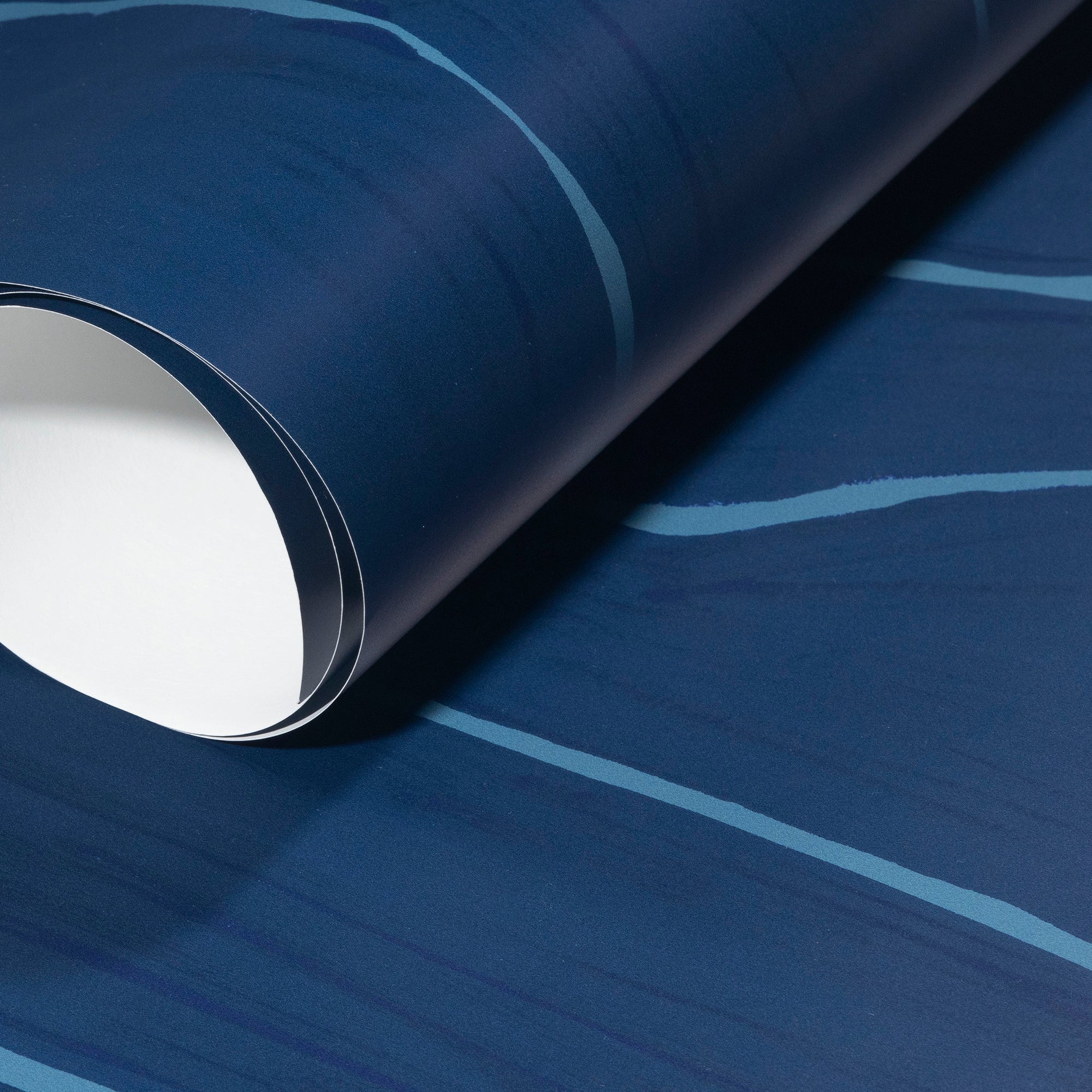Rolled-up navy blue wallpaper with fluid light blue stripes, highlighting its smooth texture and elegant design.