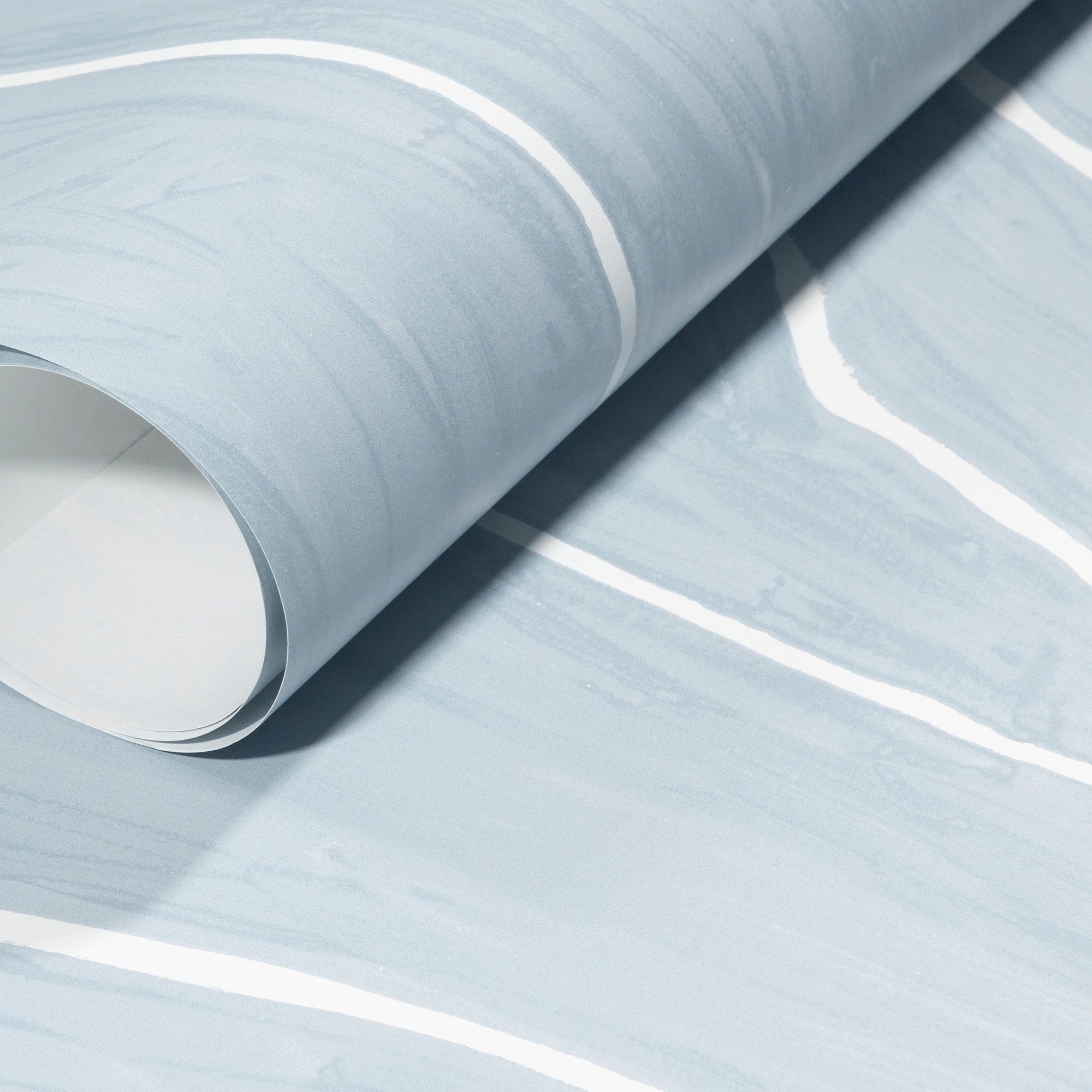 Rolled-up light blue wallpaper with delicate white wavy stripes, emphasizing its smooth texture and contemporary design.
