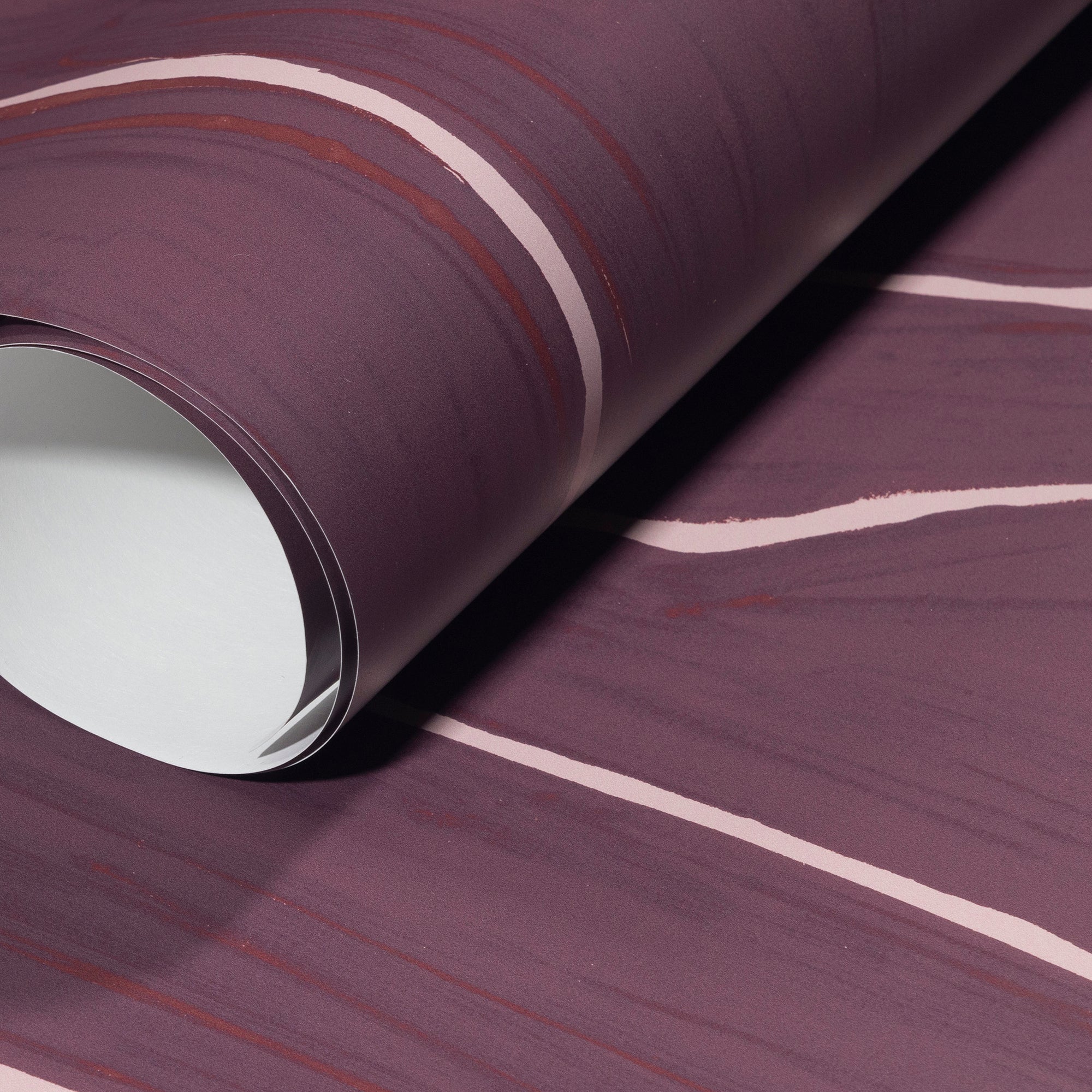Rolled-up plum wallpaper with soft pink wavy stripes, emphasizing its smooth texture and elegant contrast.