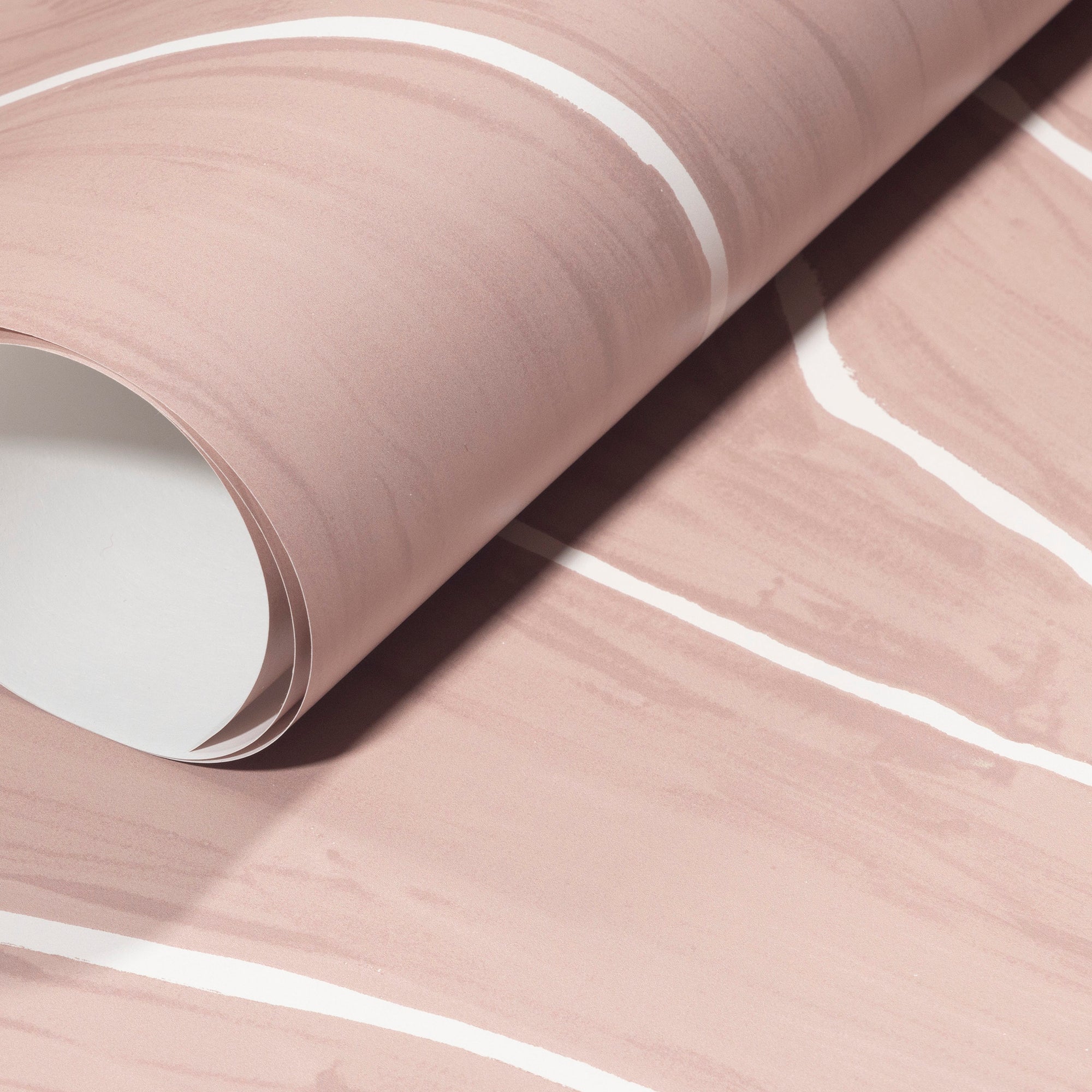 Rolled-up blush wallpaper with soft white wavy stripes, highlighting its smooth texture and sophisticated design.
