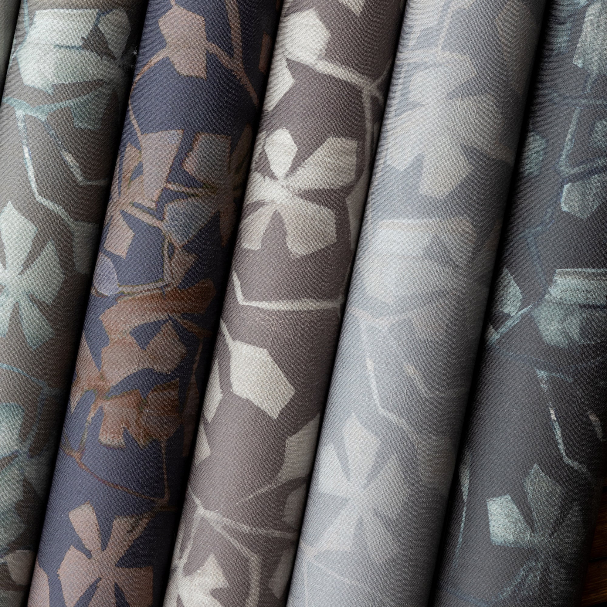 Close-up of six rolled botanical wallpaper designs in varying shades of gray, taupe, navy, and charcoal, each featuring a stylized leafy vine pattern with a matte finish.