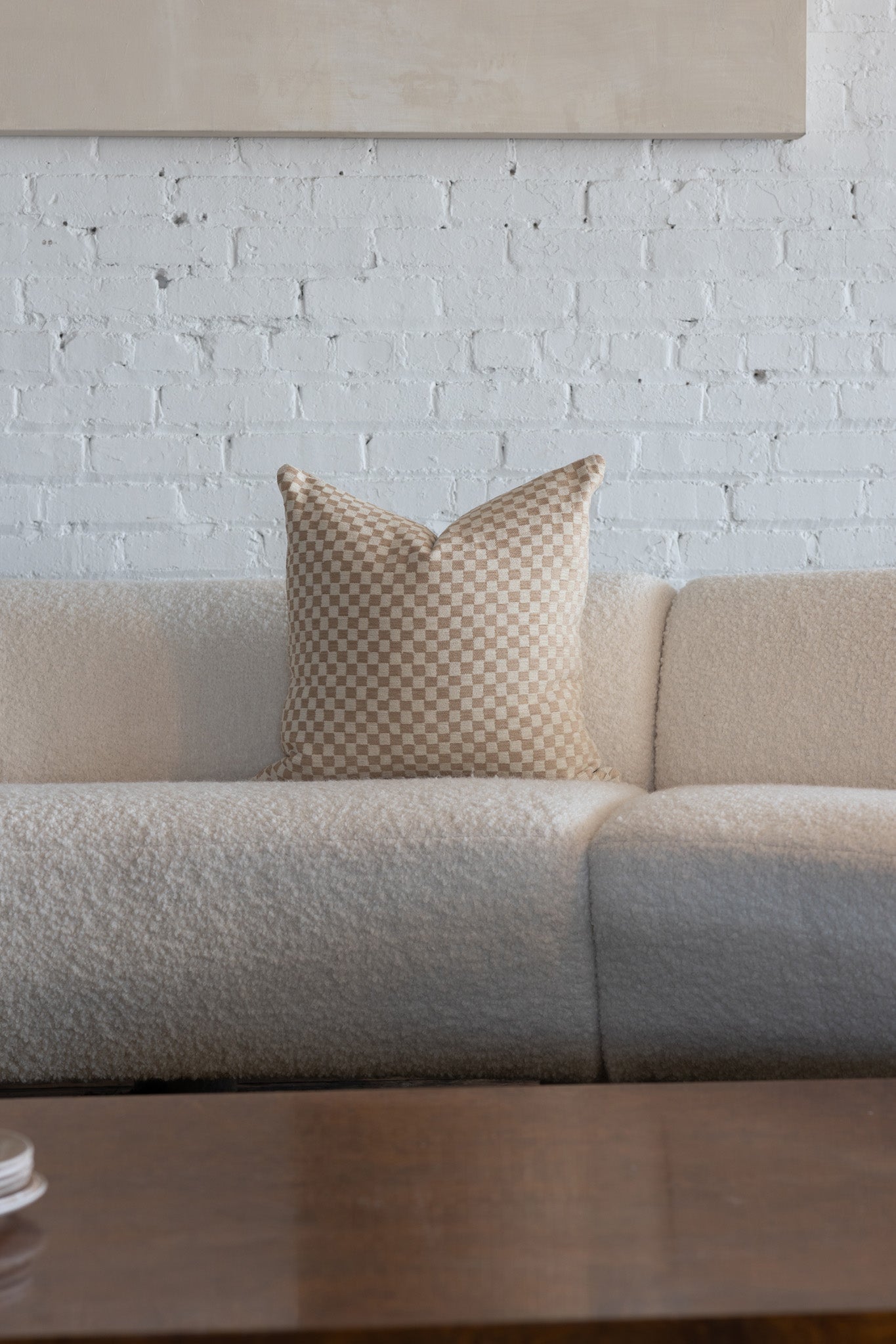 Cream and tan checkerboard throw pillow styled on white boucle sofa