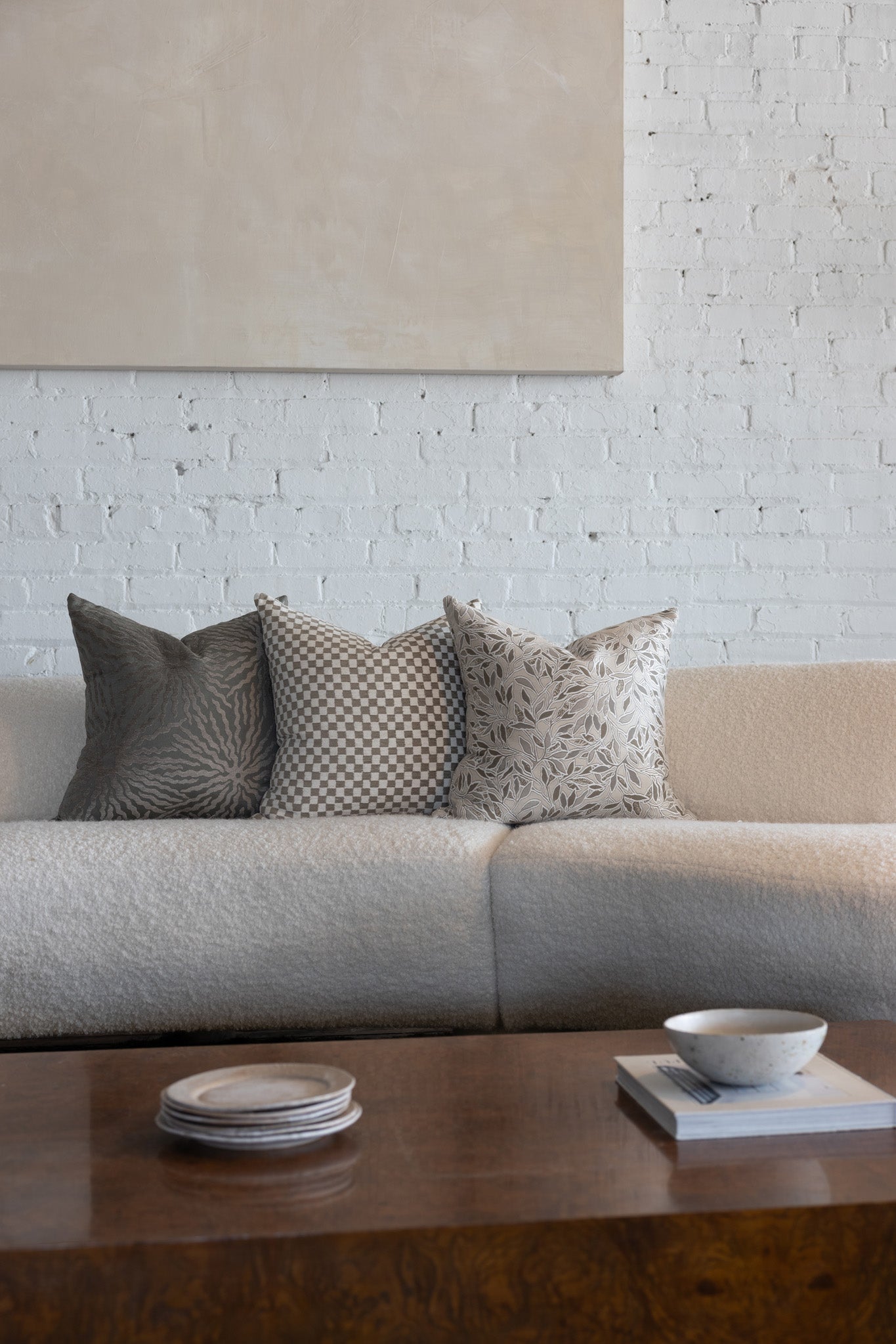 Cream and tan checkerboard pillow styled with silver gray sunburst and cream botanical leaf pillows on white boucle sofa