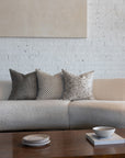 Cream and tan checkerboard pillow styled with silver gray sunburst and cream botanical leaf pillows on white boucle sofa
