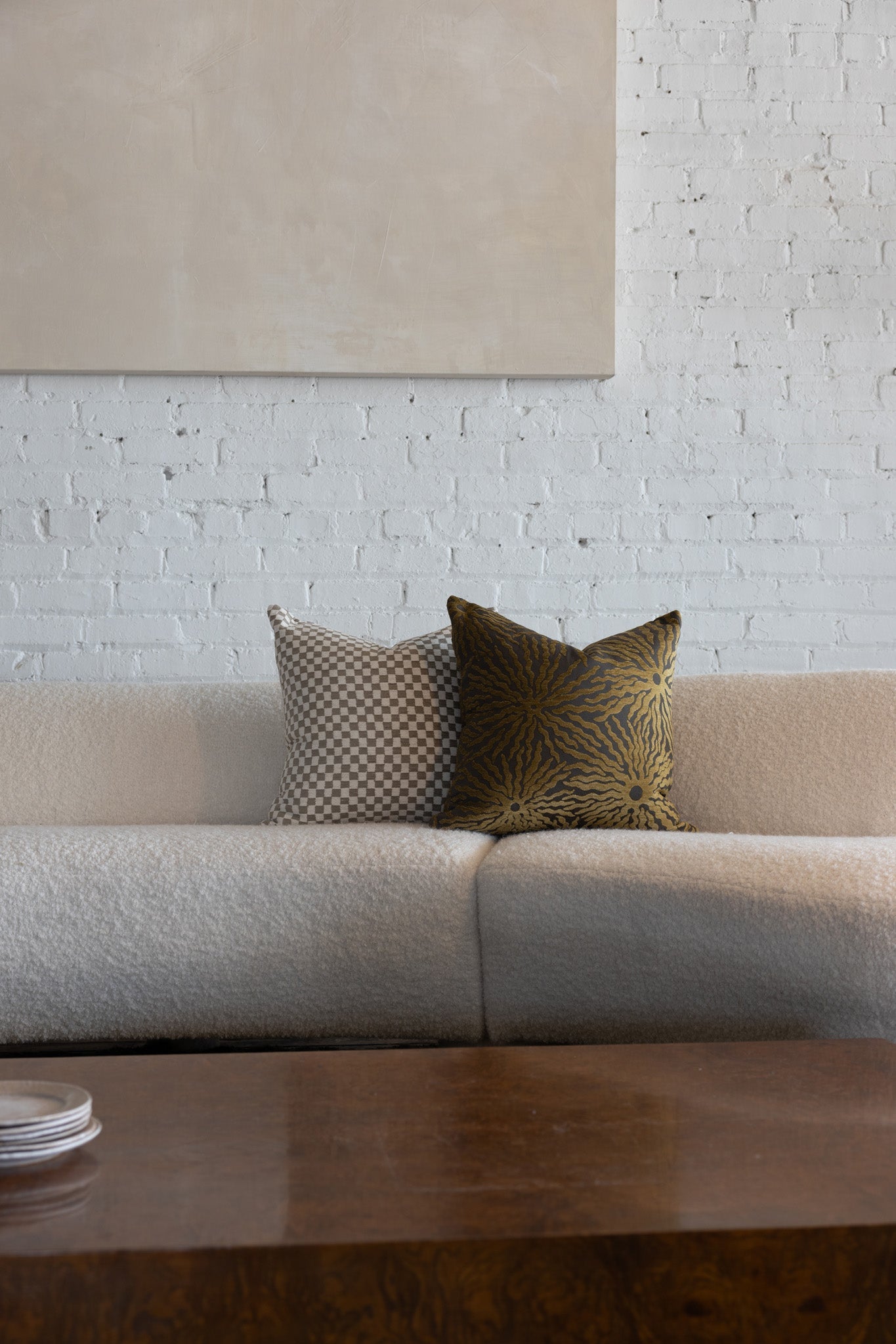 Gold and brown sunburst pillow styled with cream checkerboard pillows on white boucle sofa