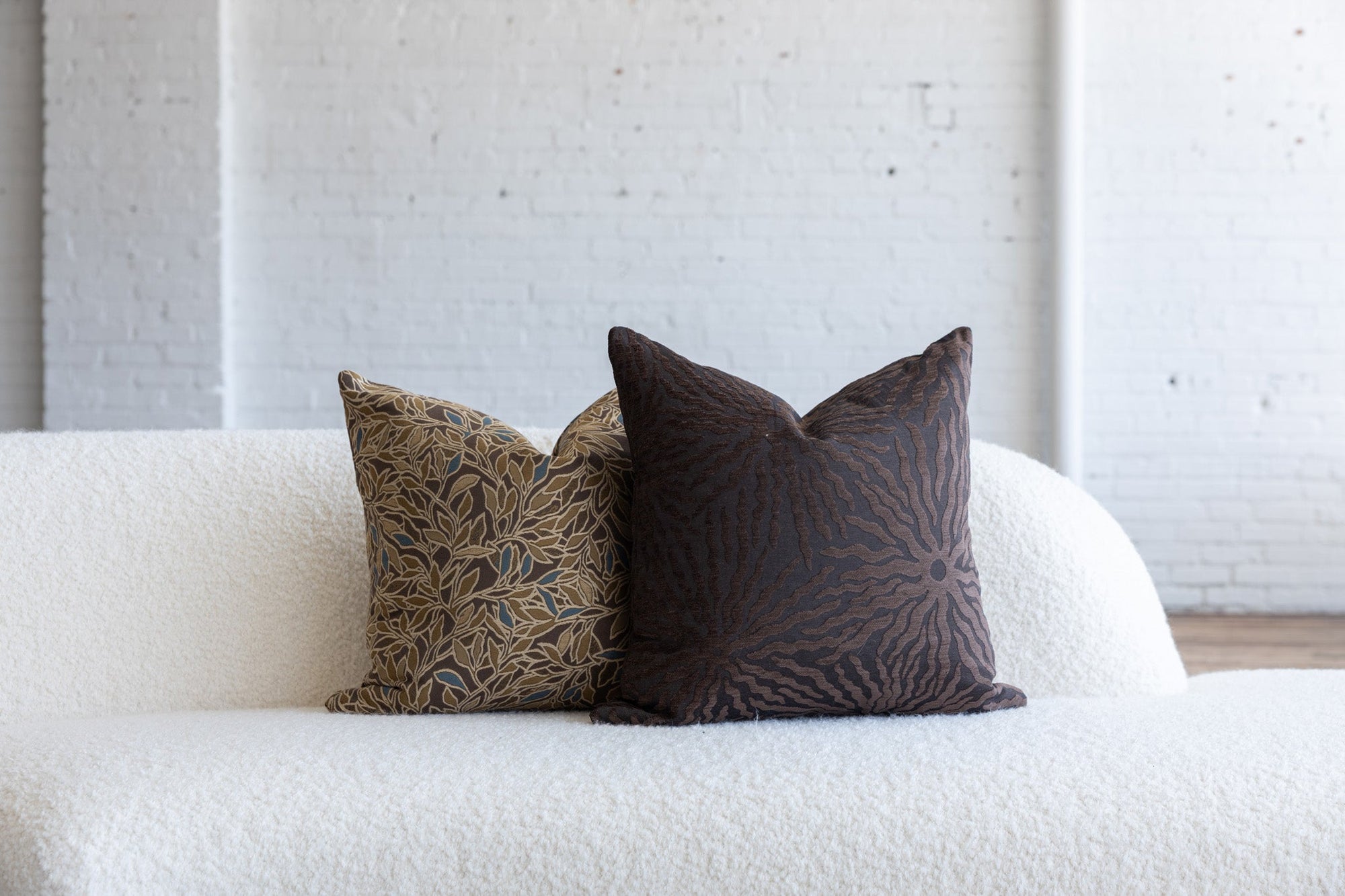 Dark brown sunburst pillow styled with dark brown botanical leaf pillows on white boucle sofa